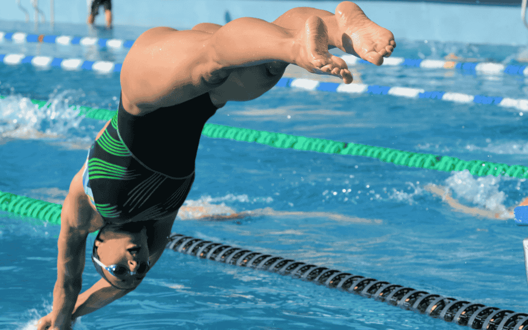 Frau springt mit einem Kopfsprung ins Wasser in einem Schwimmbad. Die Hände berühren bereits das Wasser.